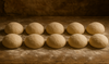 Row of raw pizza dough balls Glyphosate-free and non-GMO on a wooden surface with a dark background