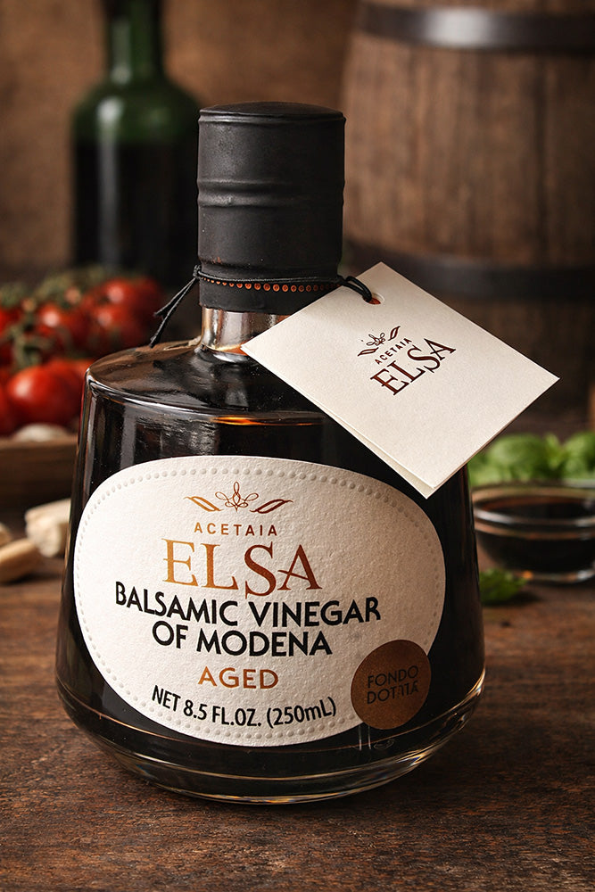 Bottle of Elsa aged Balsamic Vinegar of Modena on a wooden surface with a tag.