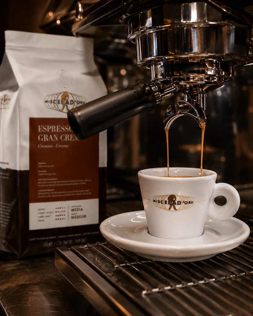 Espresso being poured into a white Miscela D'oro cup from an espresso machine, with a bag of Miscela Doro coffee in the background.