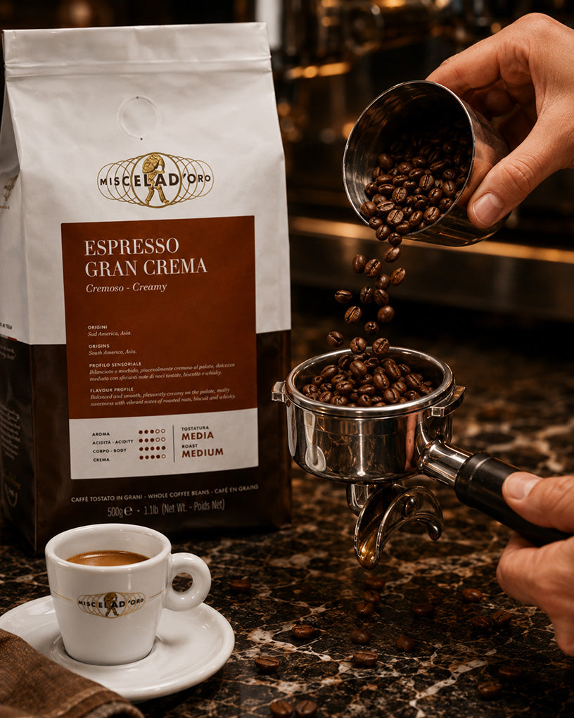 Hand pouring coffee beans into a portafilter with a bag of Miscela d'Oro Espresso Gran Crema coffee in the background.