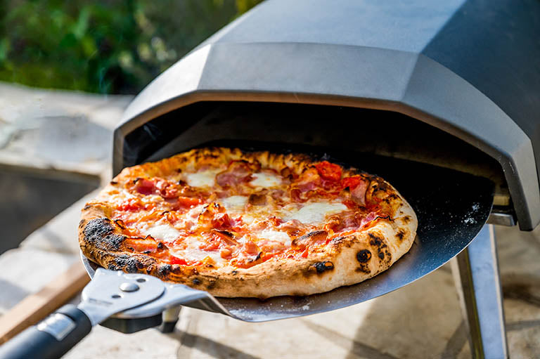 Pizza being taken out of a portable outdoor pizza oven. Ooni Frya 12 wood pellet using Frank and Sal Pizza Dough