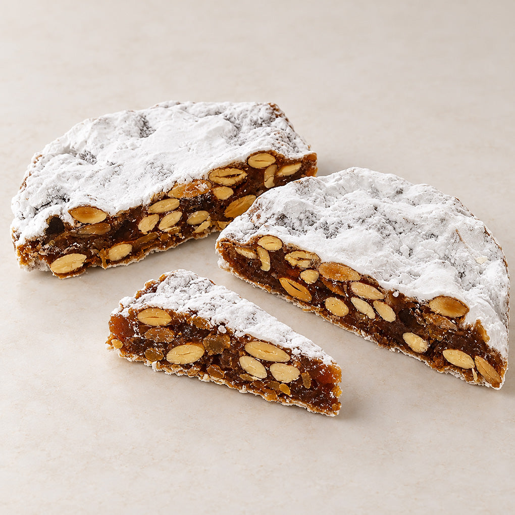 La Florentine Panforte cut open to show almonds and candied fruit beneath powdered sugar