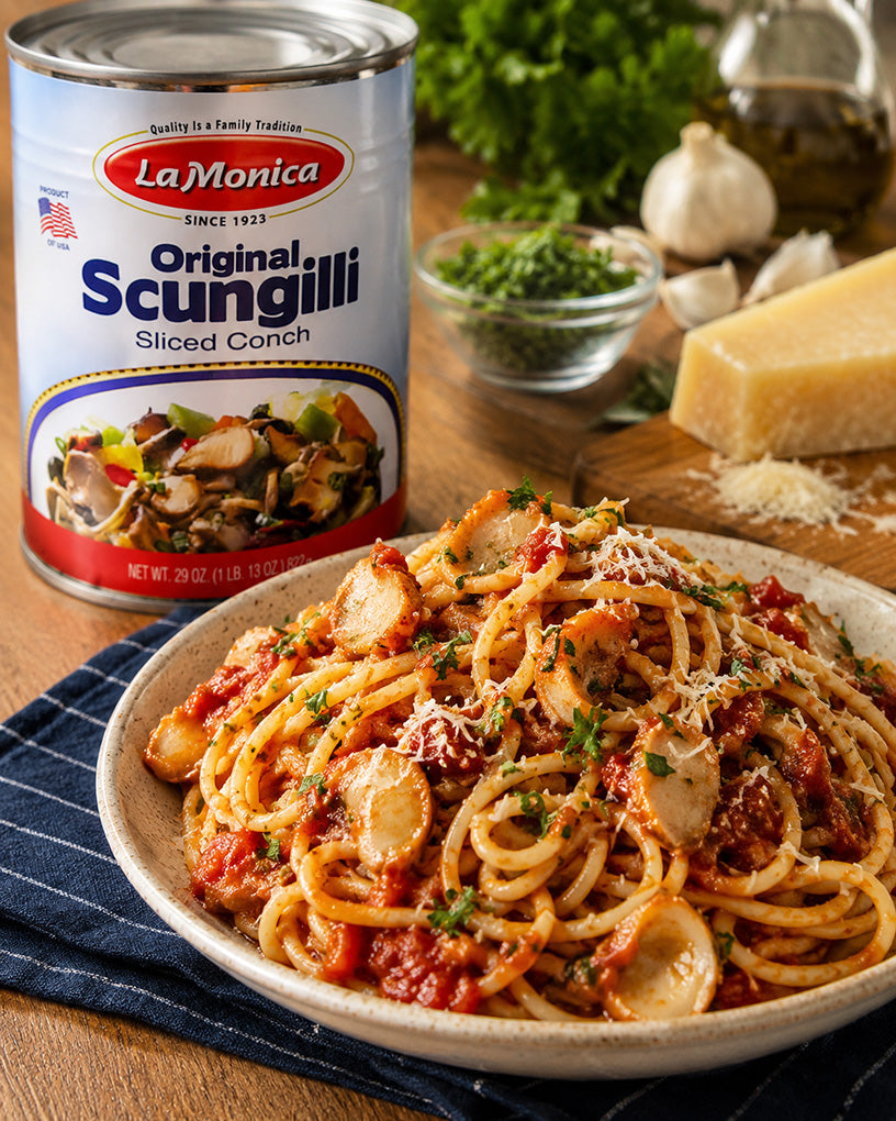 A bowl of LaMonica Original Scungilli Sliced Conch spaghetti with tomato sauce, herbs, and cheese, shown next to the can of LaMonica Original Scungilli on a wooden table.