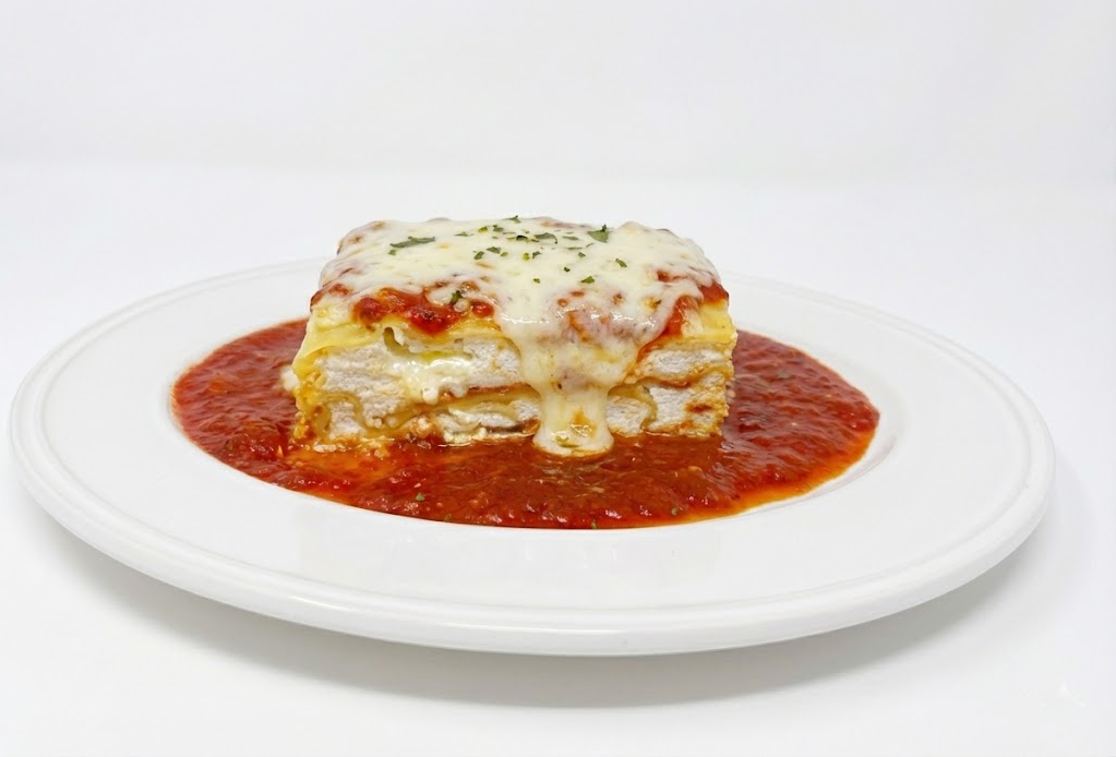 Slice of Frank and Sal lasagna on a white plate with red sauce