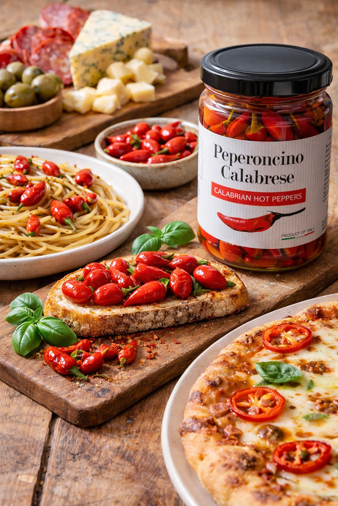 Jar of Peperoncino Calabrese on a wooden table with food items like spaghetti, bruschetta, and pizza.