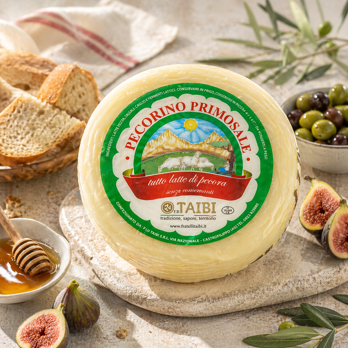 Wheel of Pecorino Primosale cheese with a green label on a stone surface with bread, olives, and figs.